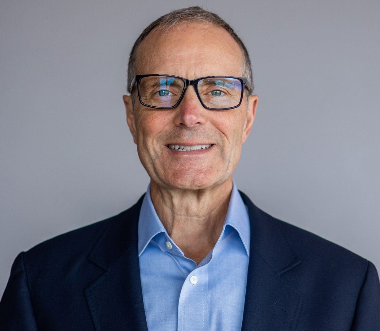 A man in glasses and a suit smiling for the camera.